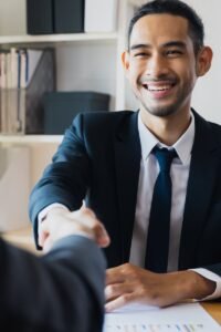 Confident businessman in suit shaking hands at office desk, symbolizing successful partnership.