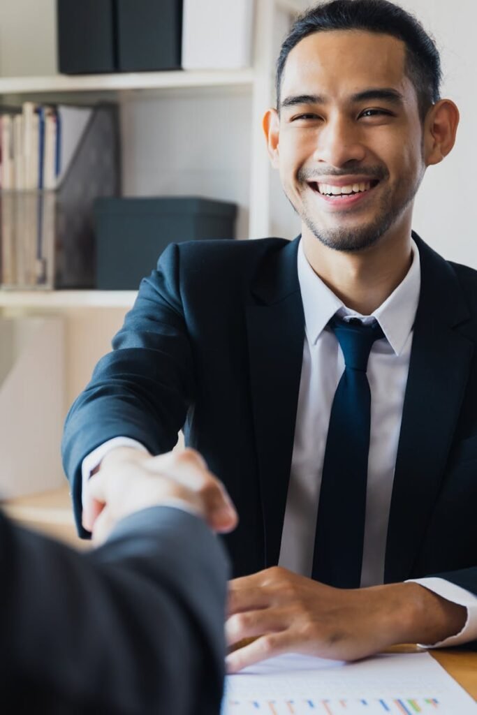 Confident businessman in suit shaking hands at office desk, symbolizing successful partnership.